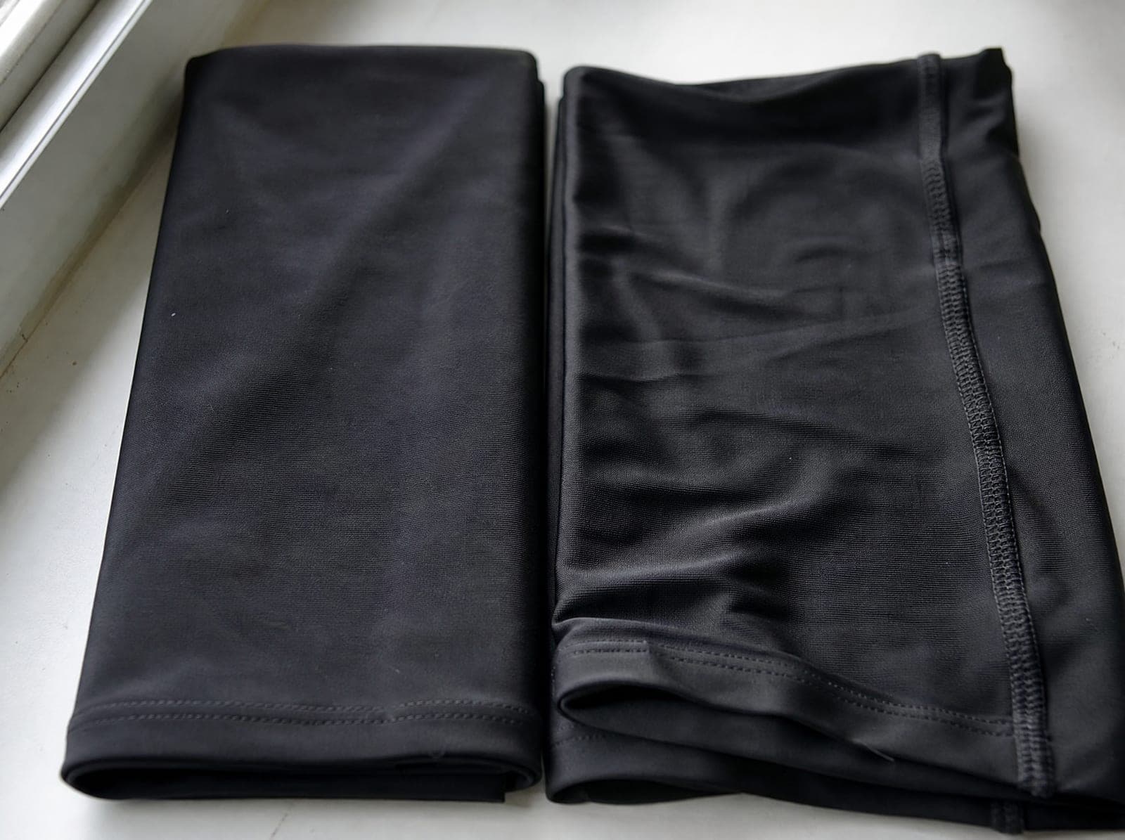 Two folded fabric swatches side by side, black nylon and black polyester, one stretched