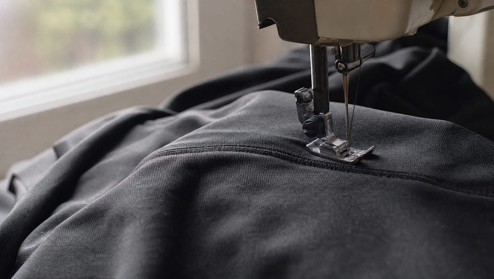 Close-up of a sewing machine needle stitching black stretch fabric, no hands