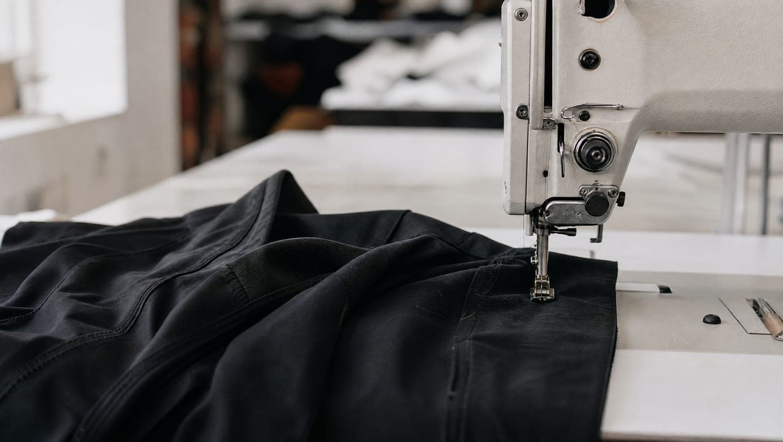 Industrial sewing machine on a clean table with a half-stitched black garment