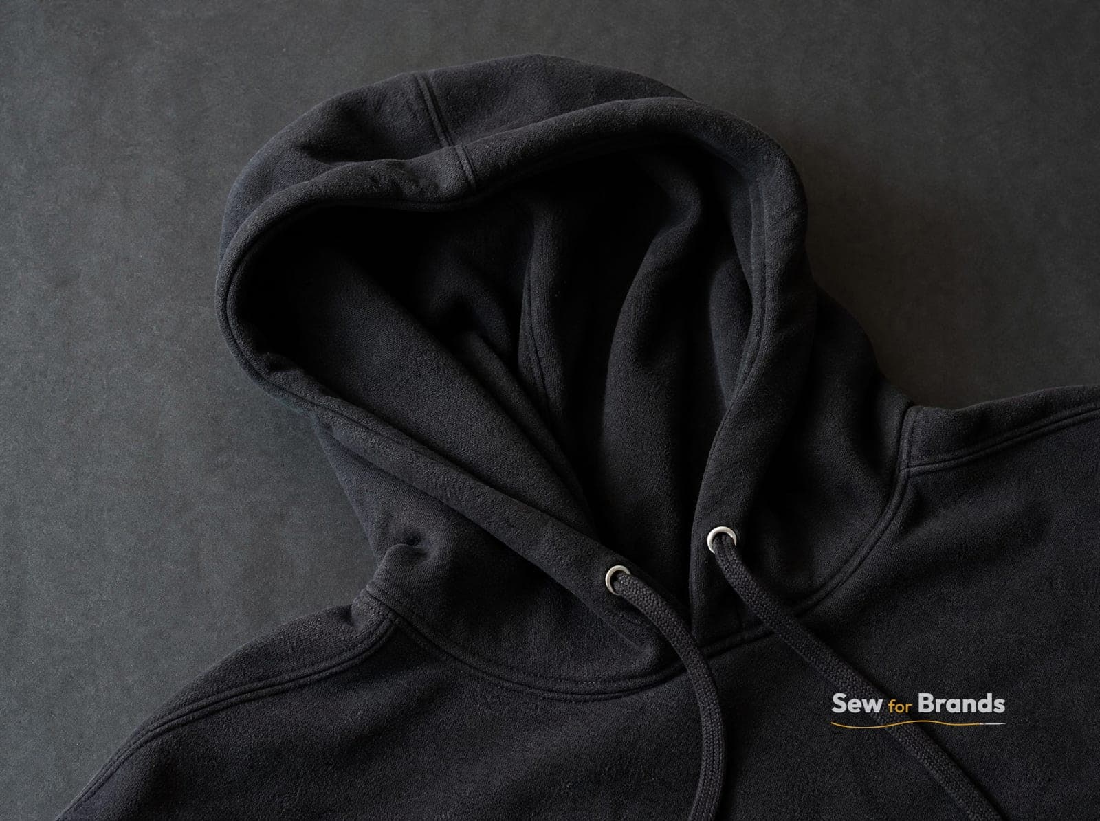Close-up of the hood and flat drawcord with metal eyelets on a black fleece hoodie