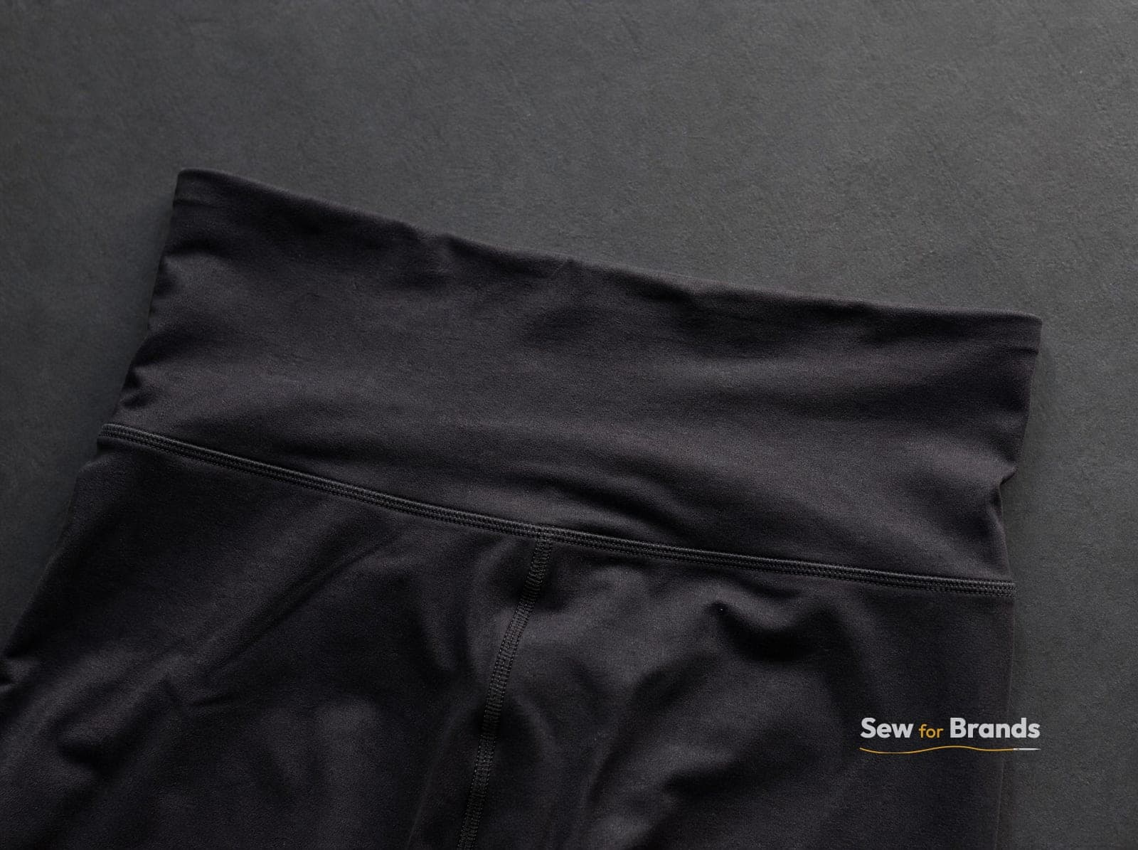 Close-up of a wide leggings waistband and flatlock seam, black brushed fabric, macro detail