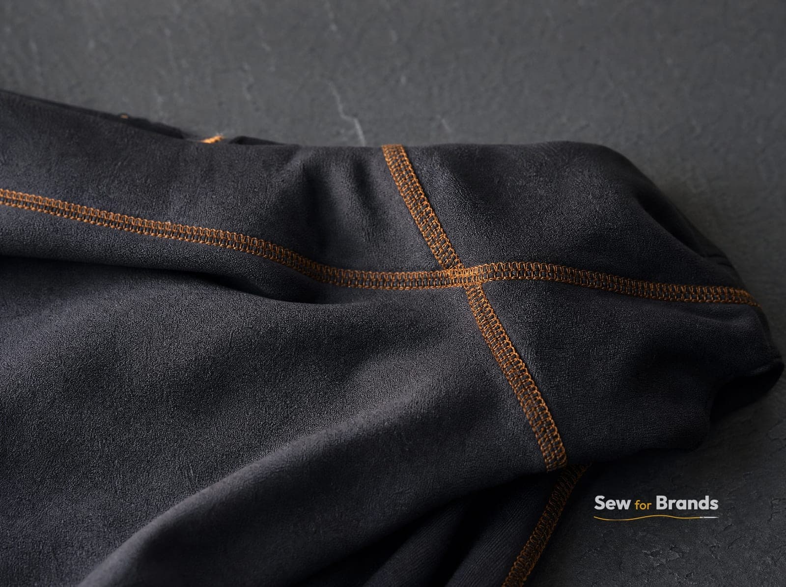 Macro of flatlock stitching on black leggings with a thin amber contrast thread