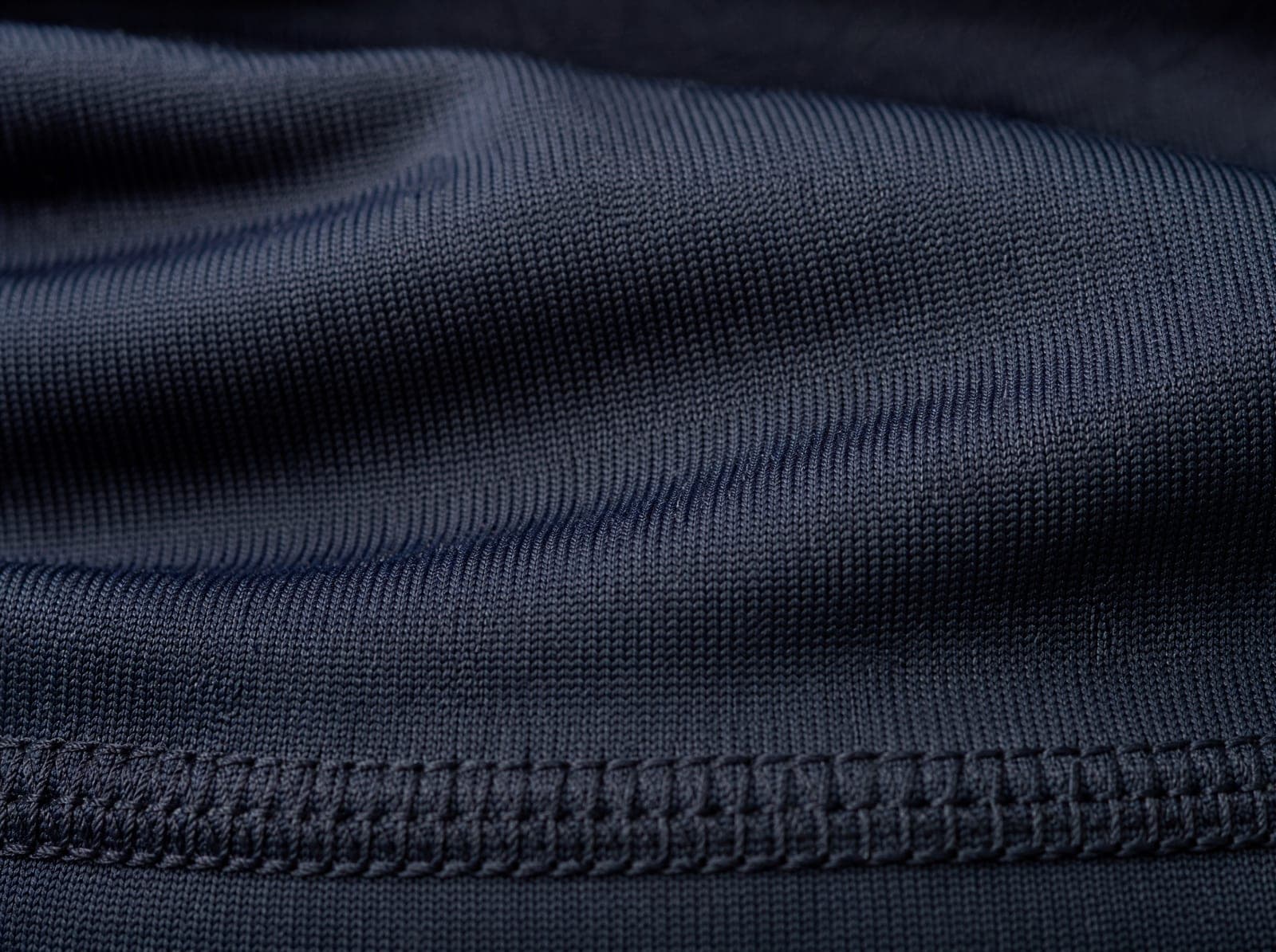 Close-up of navy compression lycra knit, fabric slightly stretched to show the weave, filling the whole frame