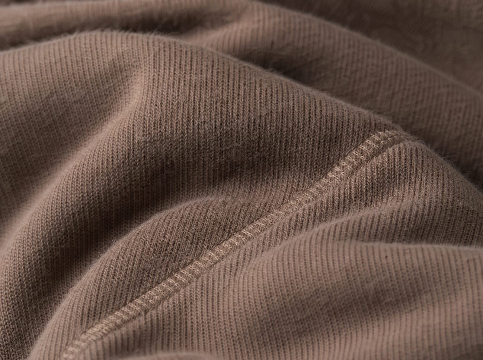 Close-up of brushed taupe cotton-poly fleece, fabric slightly stretched to show the weave, filling the whole frame