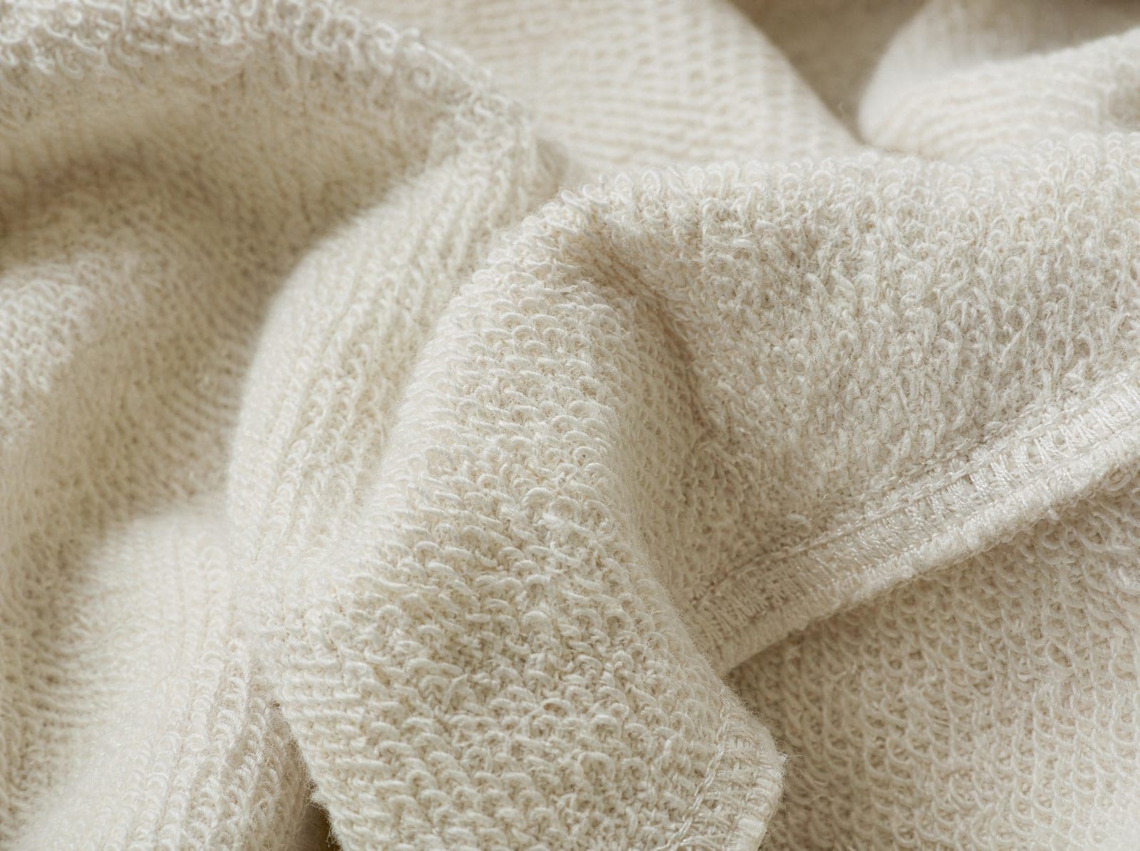 Close-up of cream French terry showing looped back, fabric slightly stretched to show the weave, filling the whole frame