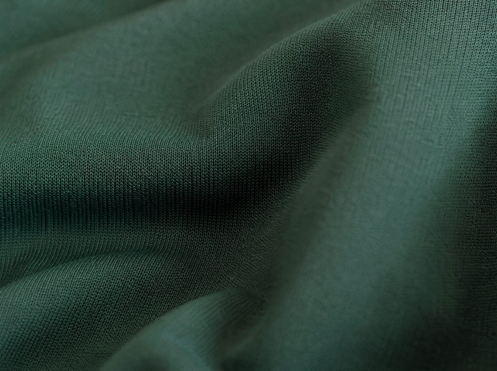 Close-up of deep green polyester-spandex interlock knit, fabric slightly stretched to show the weave, filling the whole frame