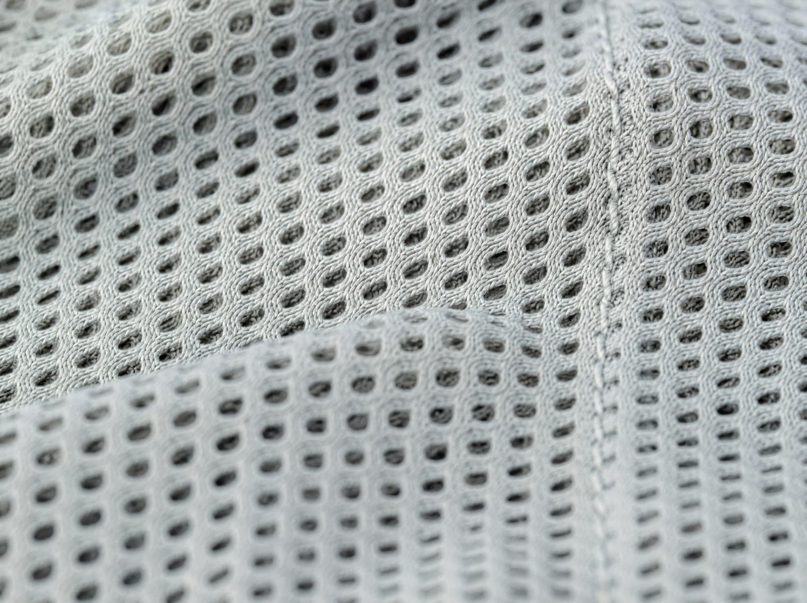 Close-up of light grey open polyester mesh, fabric slightly stretched to show the weave, filling the whole frame