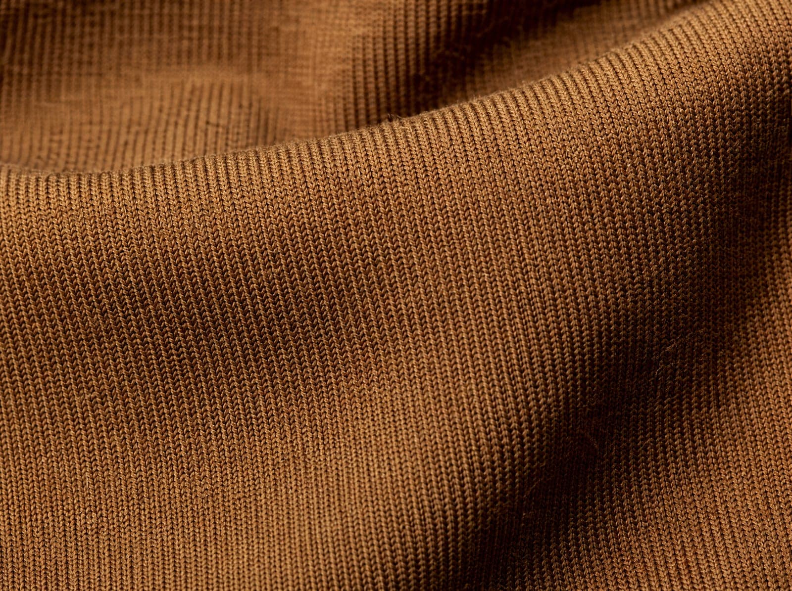 Close-up of warm brown recycled polyester-spandex knit, fabric slightly stretched to show the weave, filling the whole frame